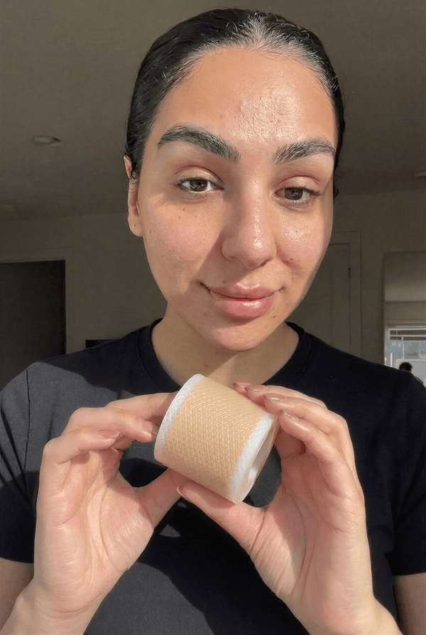 Kvinna håller upp en rulle medicinsk silikontejp från Sera Vale framför ansiktet i naturligt dagsljus.
