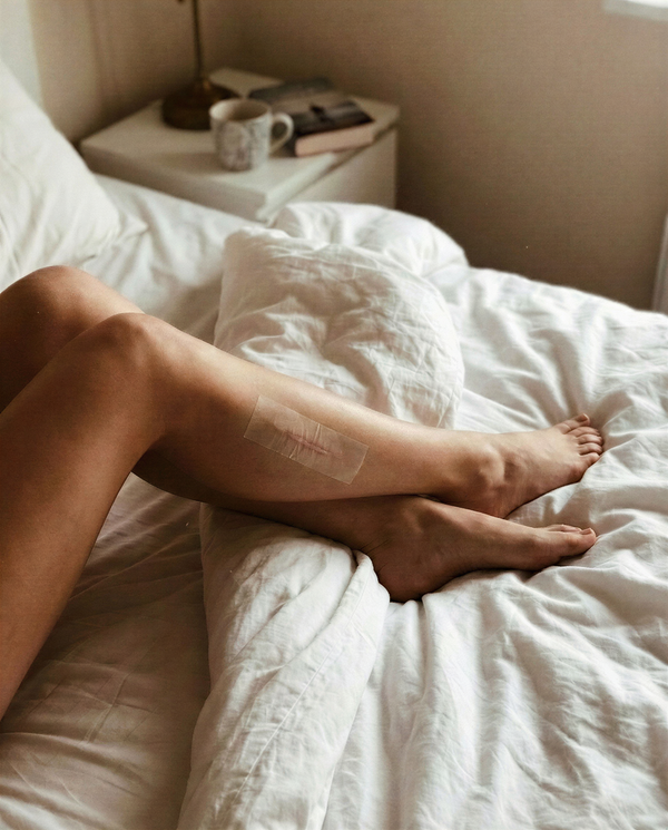 Person ligger i säng med silikontejp applicerad på underbenet för ärrbehandling